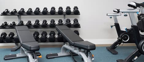 A gym with two benches, a wall of dumbbells, and a stationary bike.