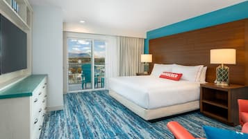 A hotel room with a large bed, a desk, a chair, and a view of mountains through the balcony doors.
