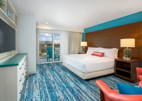 A hotel room with a large bed, a desk, a chair, and a view of mountains through the balcony doors.