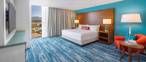 Habitación de hotel con una cama grande, vista a la ciudad, alfombra azul y una silla roja.