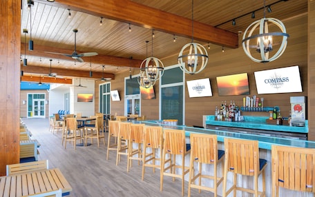 A bar area with wooden chairs and tables, a bar counter with bottles, and a ceiling fan.