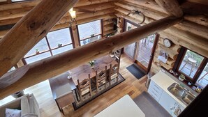 Ein geräumiges Loft mit freiliegenden Holzbalken, einem zentralen Essbereich und einer Küche mit großem Fenster.