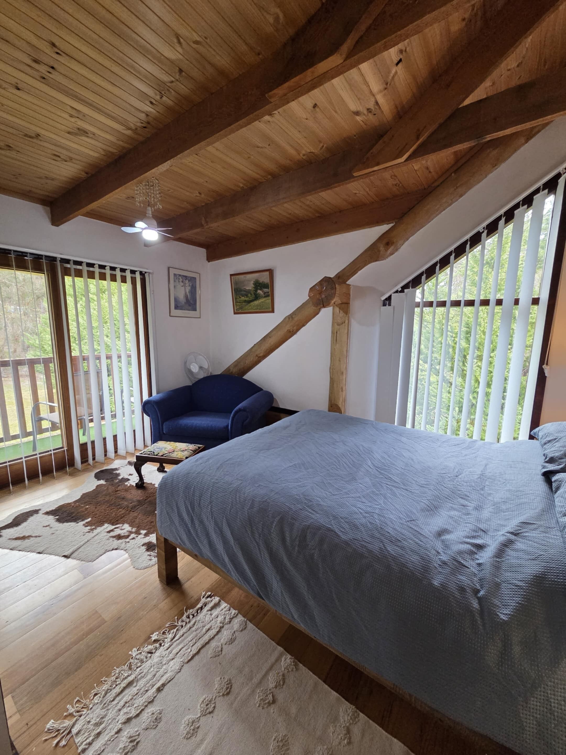 Un dormitorio con cama, una silla, un ventilador y una ventana con persianas.