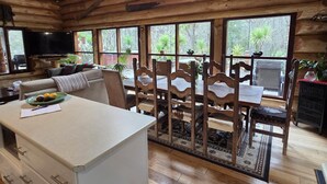 Ein rustikales Blockhaus-Interieur mit Küche, Essbereich und großen Fenstern.