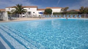 Piscina transparente com espreguiçadeiras e um edifício ao fundo.