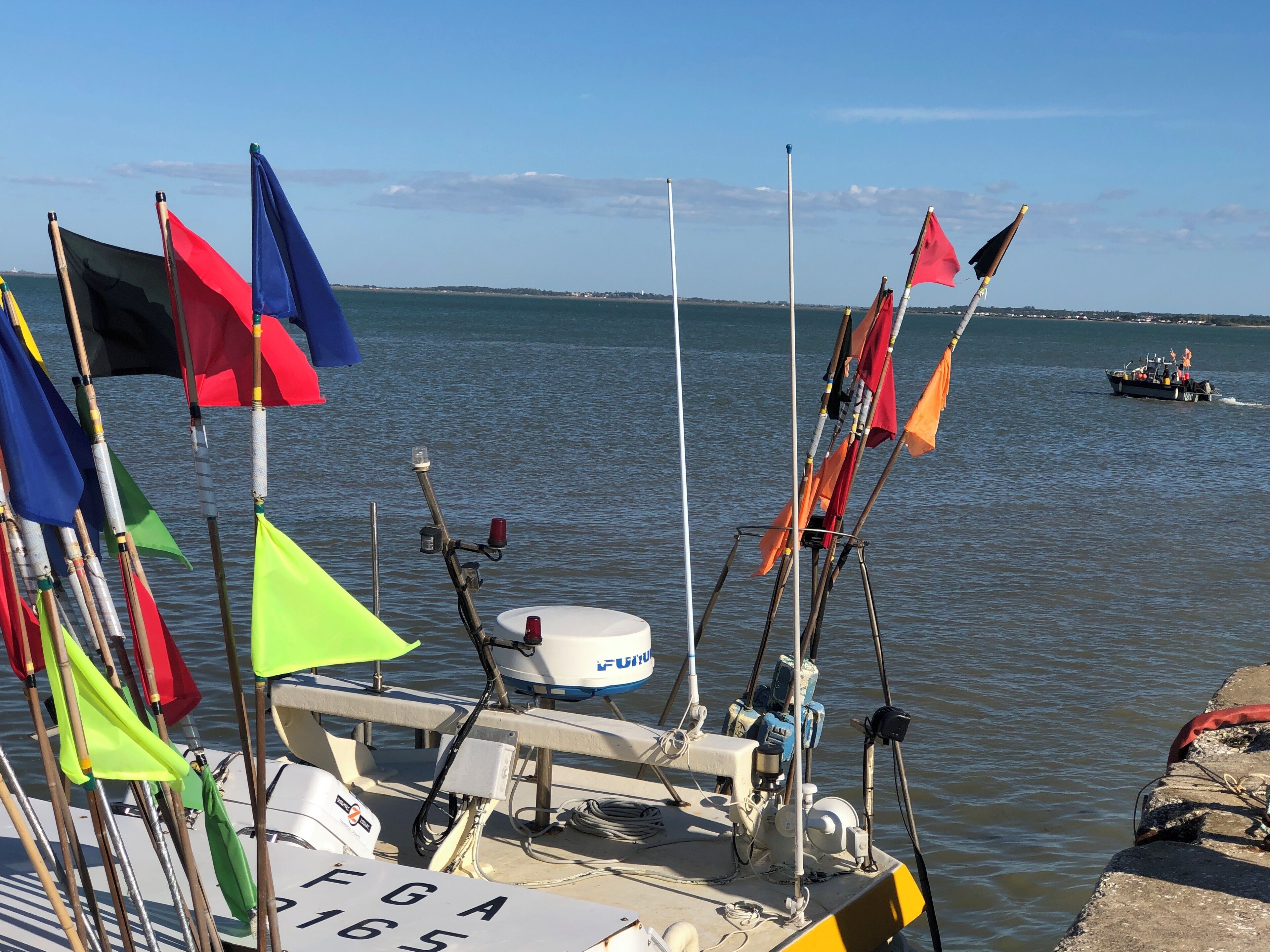 A boat docked at a pier with multiple flags and a motor in the foreground.