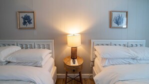 Une chambre d’hôtel avec deux lits, une table de chevet en bois avec une lampe et deux œuvres d’art encadrées accrochées au mur.