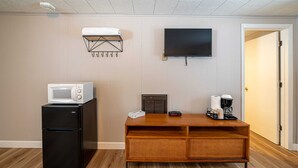 Une petite cuisine équipée comprenant un four à micro-ondes, un réfrigérateur et une machine à café, le tout installé sur un meuble en bois. Un téléviseur à écran plat est fixé au mur, et une porte donne accès à une autre pièce.