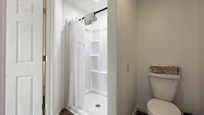 Casa de banho com chuveiro, sanita e porta para outro quarto.