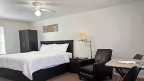 Una camera d'hotel con un letto, una scrivania, una sedia, una lampada e una ventola a soffitto.