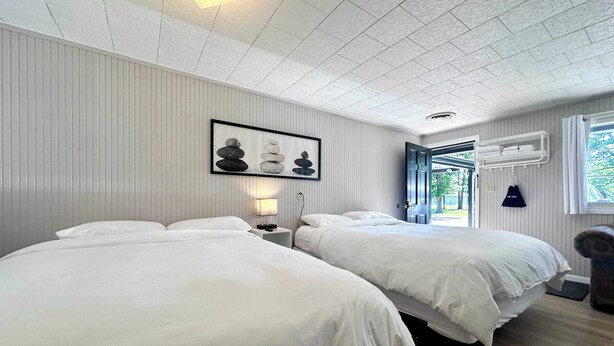 Une chambre d’hôtel avec deux lits, un luminaire au plafond, un tableau encadré, une table de chevet, une fenêtre et une porte donnant sur l’extérieur.
