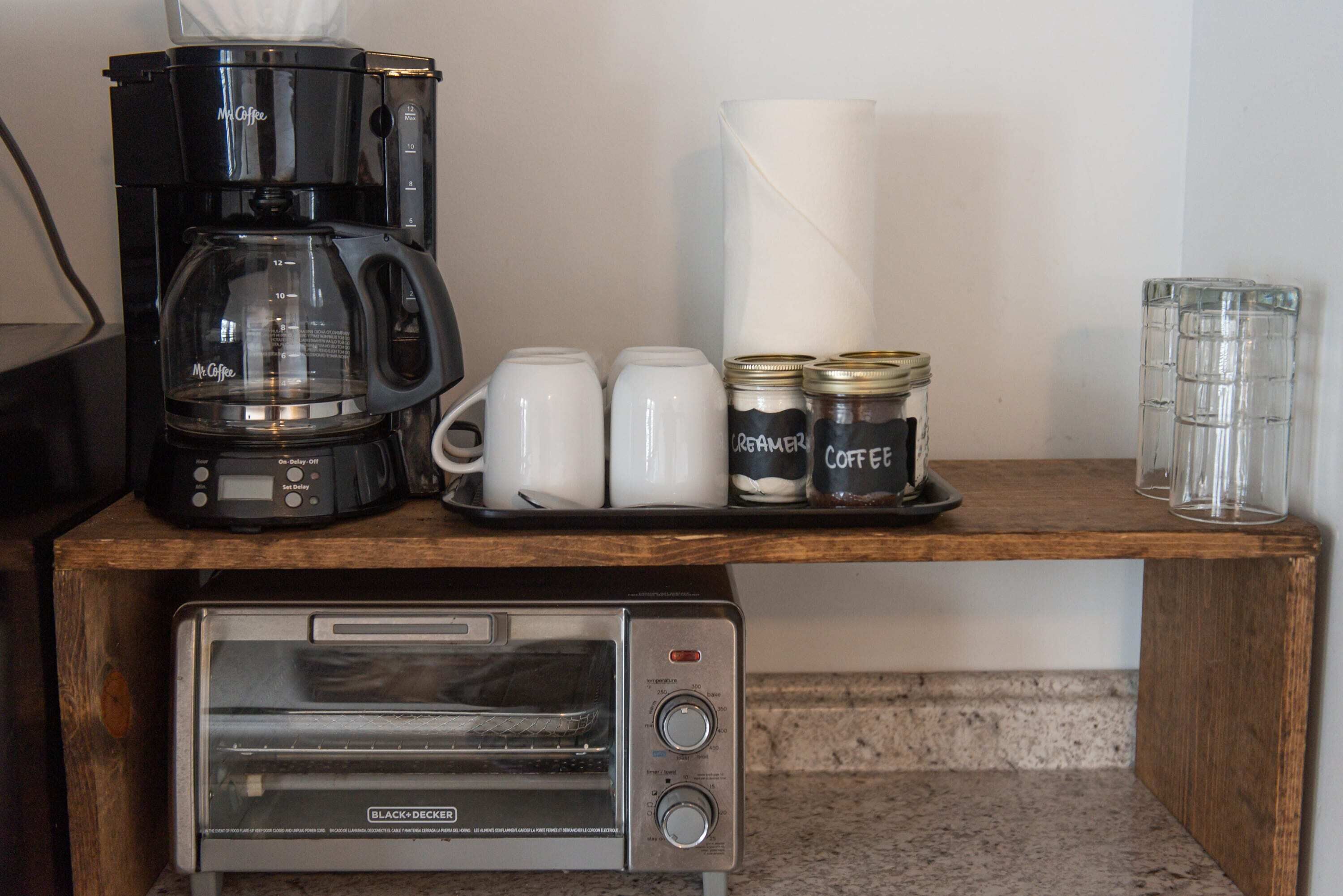 A kitchenette with a coffee maker, two mugs, two jars labeled "cream and coffee," and a toaster.