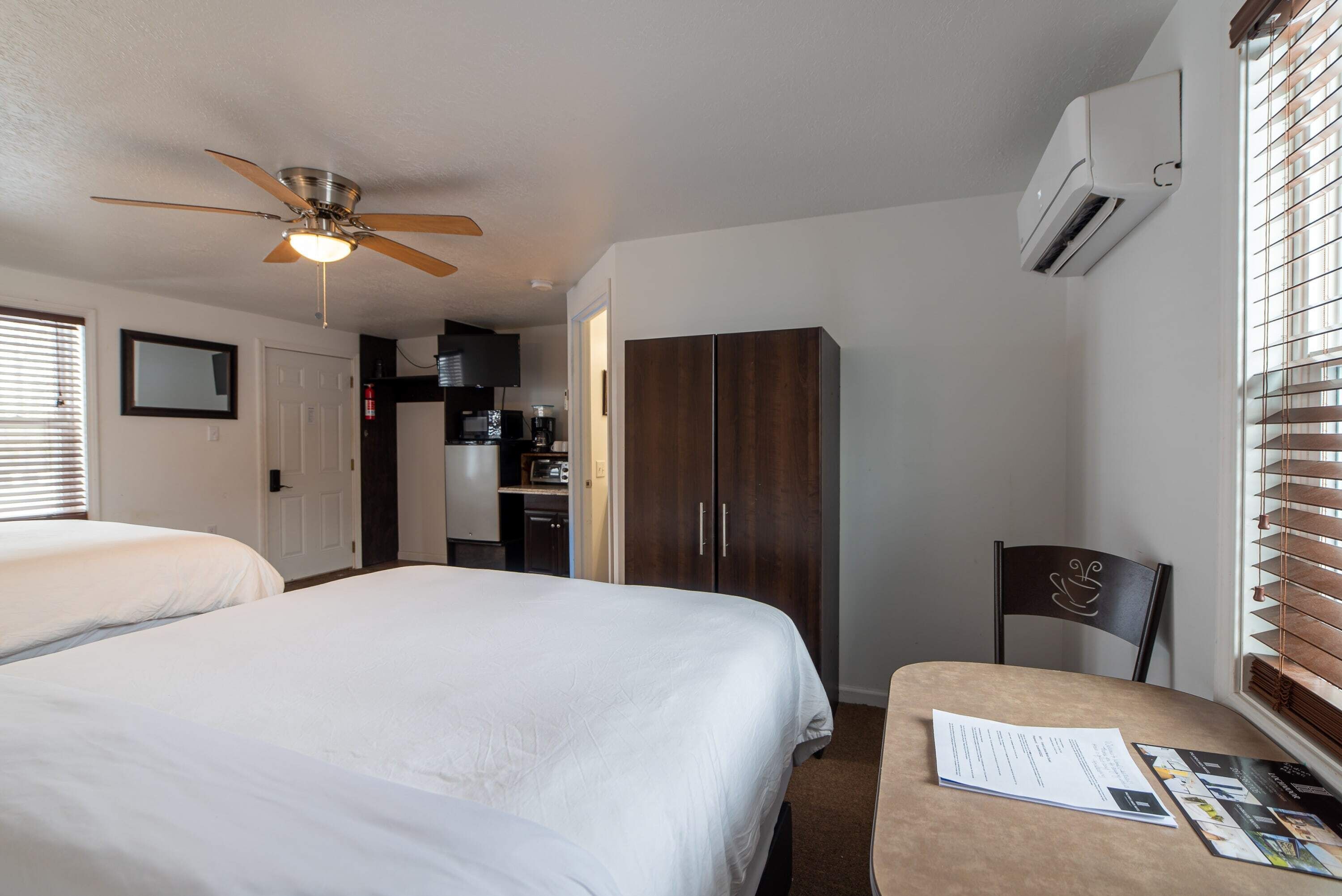 Une chambre avec deux lits, un ventilateur de plafond, une armoire et une table avec une chaise.