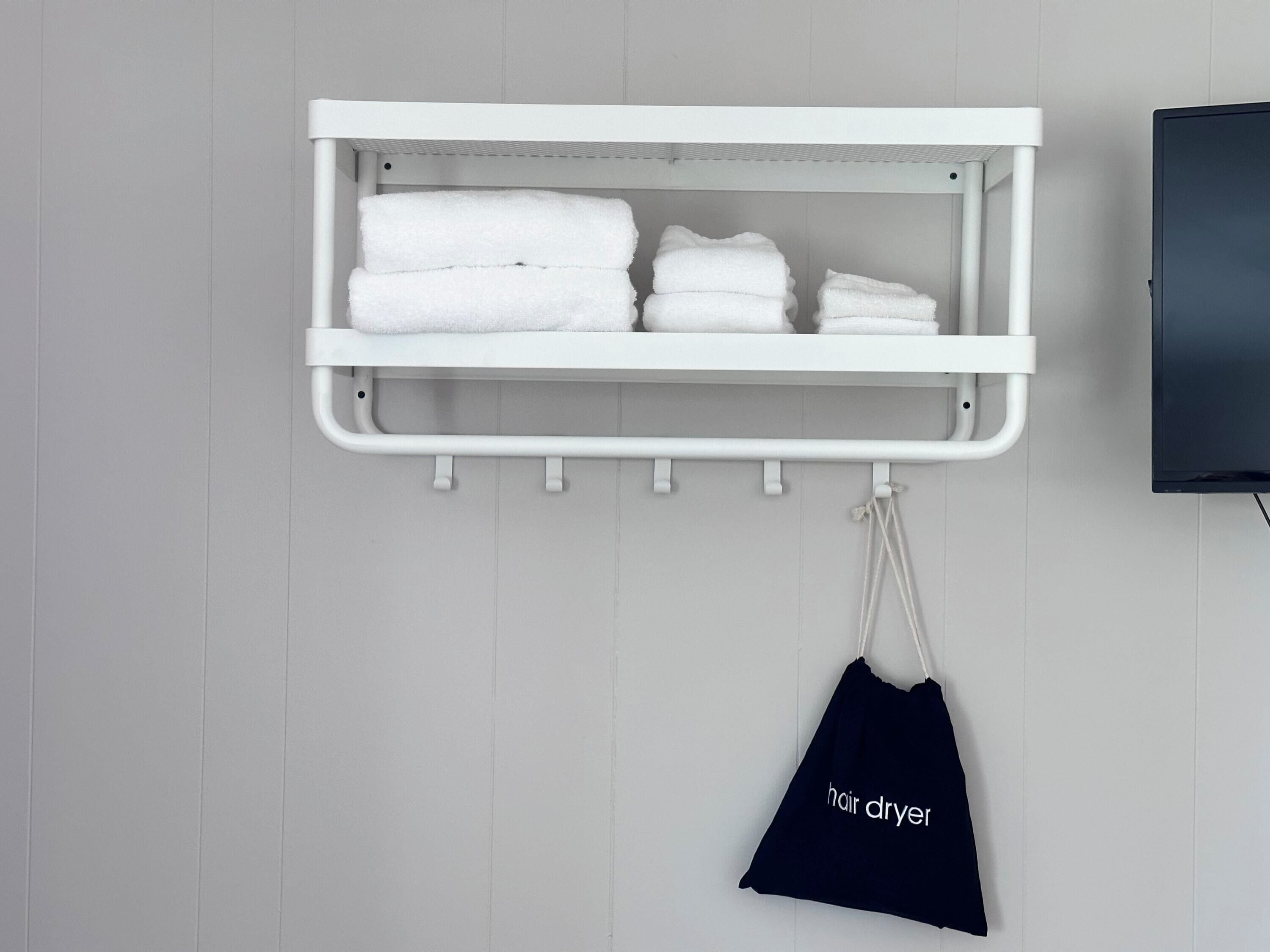 Een witte handdoekhouder met handdoeken en een tas voor een haardroger.