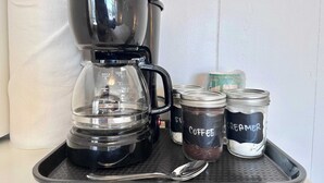 Een koffiezetapparaat met een glazen kan en een plank met twee gemarkeerde potten, één voor koffie en één voor room.