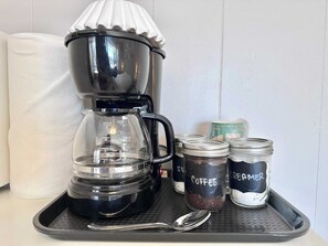 Eine Kaffeemaschine mit Glasbehälter und einer Ablage mit zwei beschrifteten Gläsern, eines für Kaffee und eines für Sahne.