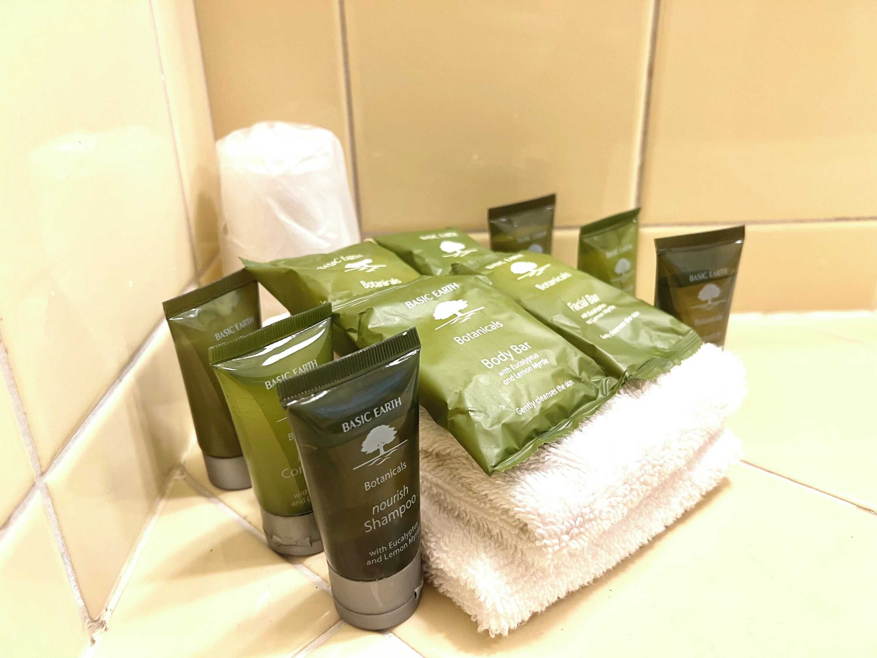 Een badkamerplank met diverse toiletartikelen, waaronder een groene fles met de tekst 'Botanical Body Bar' en een witte handdoek.