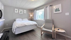A bedroom with a bed, a chair, a desk, and a window with curtains.