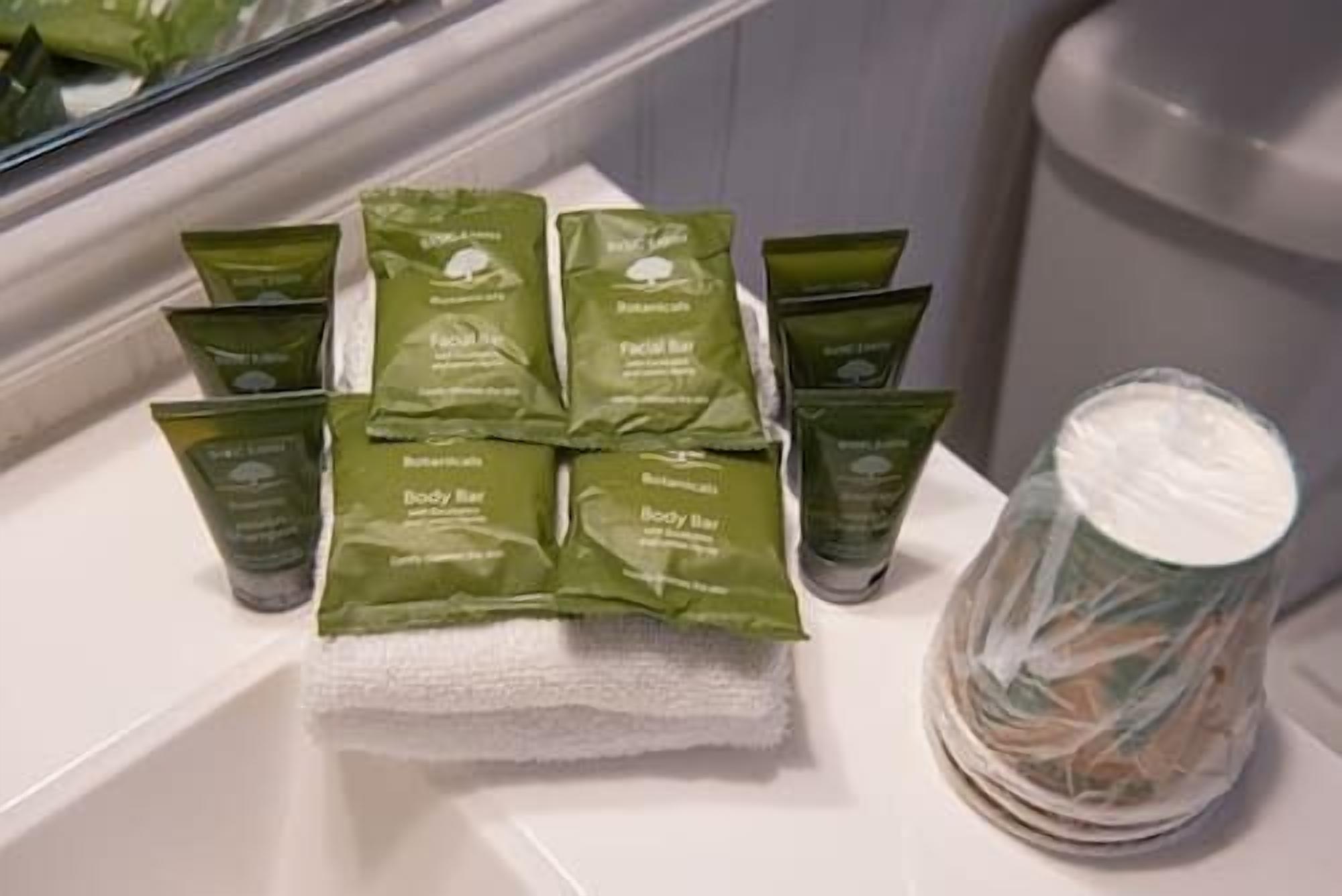 Une salle de bain avec un porte-serviettes sur lequel sont posés plusieurs emballages de savons verts et un récipient transparent en plastique avec un couvercle blanc.