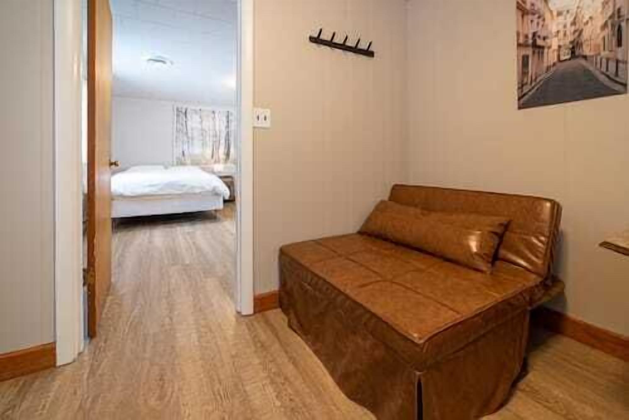 Een slaapkamer met een bruine slaapbank, een houten vloer, een bed op de achtergrond en een wandhaak.