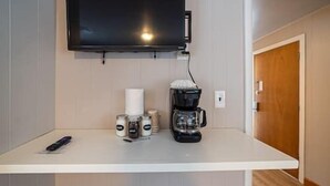 Een kleine kitchenette met een koffiezetapparaat, potjes met kruiden, een afstandsbediening en een aan de muur bevestigde televisie.