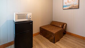 A compact kitchenette with a black refrigerator and a white microwave, a brown leather sofa, and a framed picture on the wall. - Star Gate Room 14 Indian River, MI (Indian River)