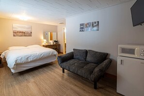 A hotel room with a bed, a sofa, a microwave, a small table with a lamp, and a mirror.