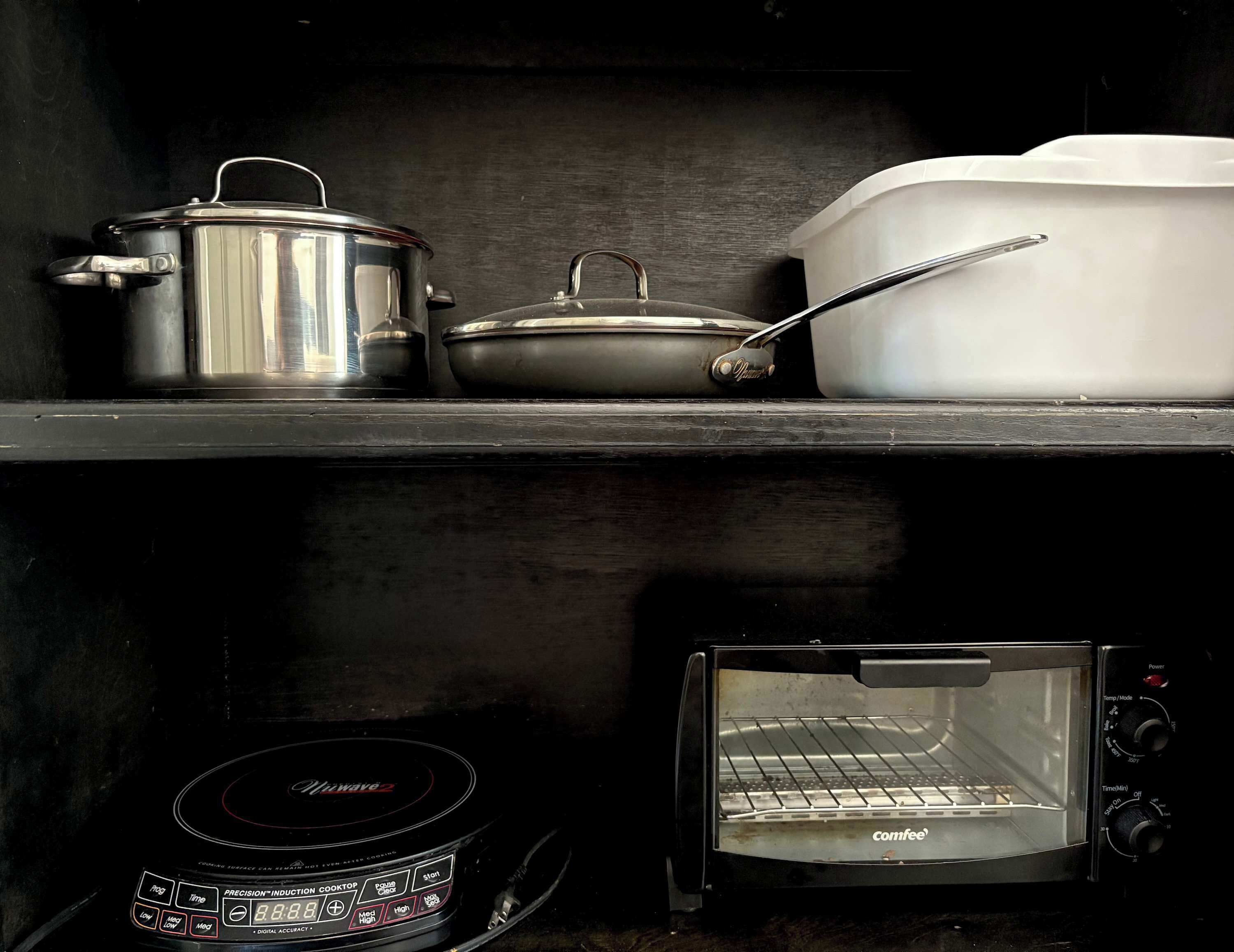 A kitchen shelf with a pot, a pan, and a white container. Below, a toaster oven is visible.