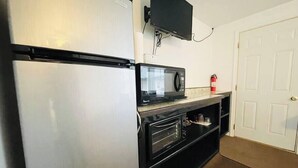 A compact kitchen with a refrigerator, microwave, oven, and a flat-screen TV mounted on the wall. - Room 6 at Inland Lakes Motel, Indian River, MI (Indian River)