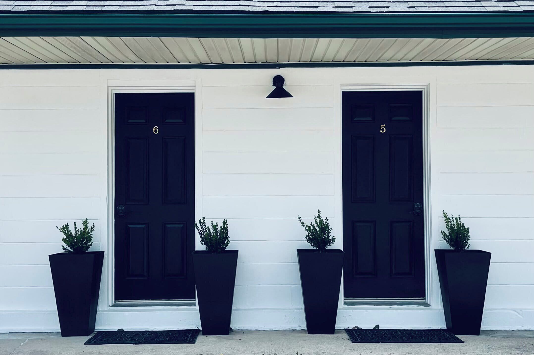 A white building with two black doors labeled 6 and 5, flanked by black planters.