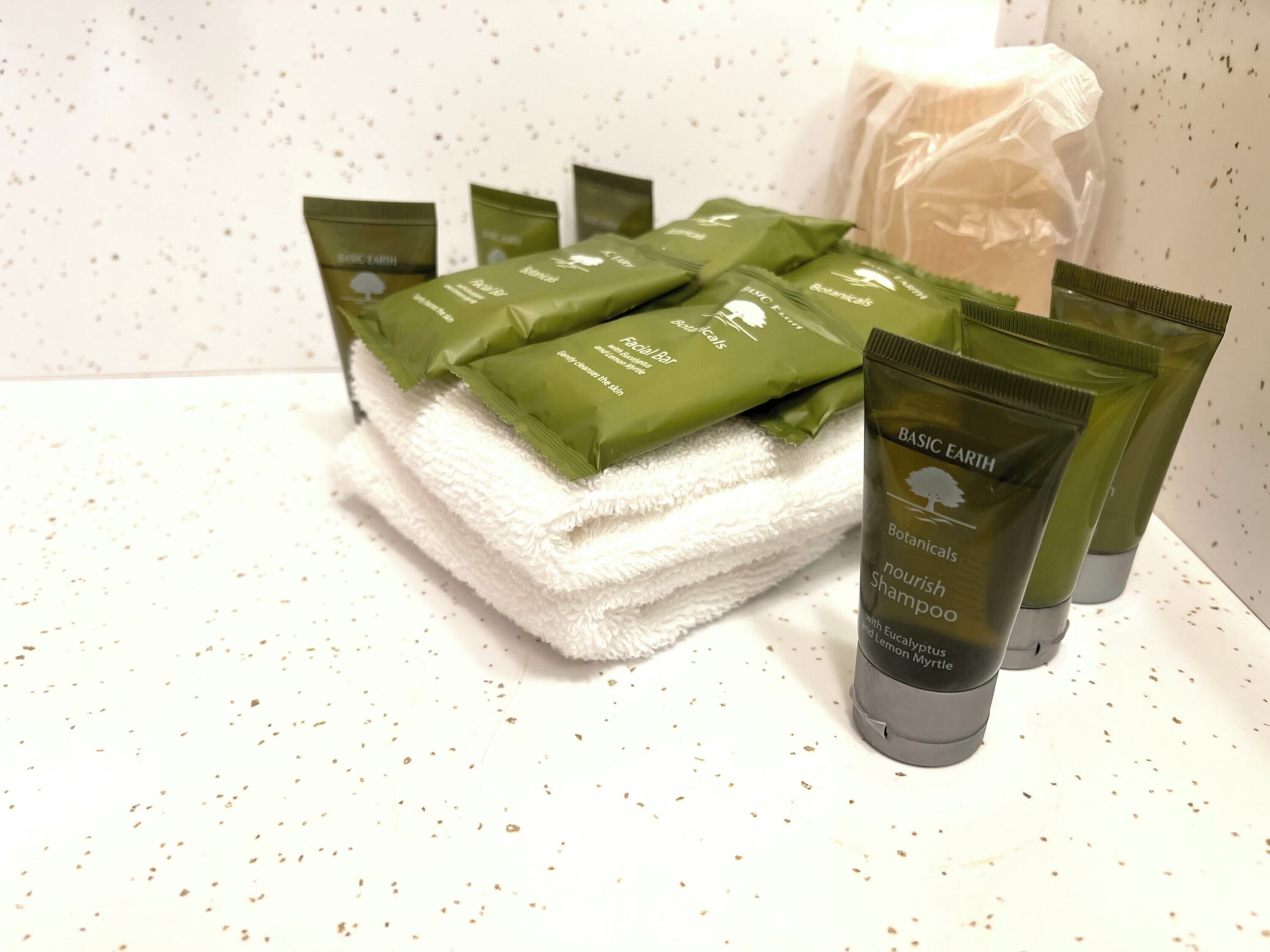 A stack of green botanical skincare products and a white towel on a speckled white surface.