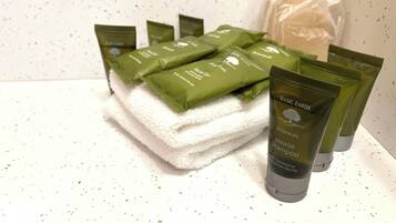 A stack of green botanical skincare products and a white towel on a speckled white surface.