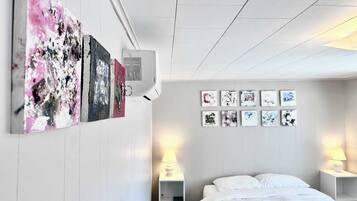 Una camera d'albergo con un letto, pareti bianche e opere d'arte alle pareti.