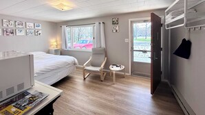 Pieni hotellihuone, jossa on sänky, tuoli, pieni pöytä ja ikkuna, josta on näkymä ulkona olevaan punaiseen autoon.