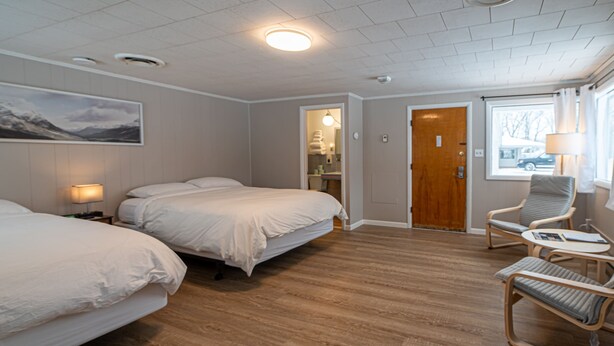 Ein Hotelzimmer mit zwei Betten, einem Sessel, einem Tisch, einer Tür und einem Fenster.