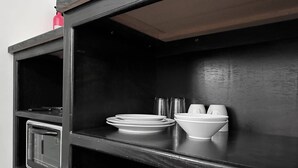 Un mobiletto in legno nero con un forno a microonde e un piccolo forno. Si notano piatti, ciotole e tazze bianche sullo scaffale.