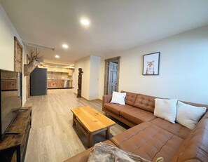 Un salón con un sofá de cuero marrón, una mesa de centro de madera y un trofeo de venado colgado en la pared.