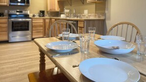 Una cocina moderna con armarios de madera, electrodomésticos de acero inoxidable y una mesa de comedor dispuesta con platos y vasos.