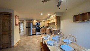 Una cocina moderna con armarios de madera, horno empotrado y refrigerador. Hay una mesa de comedor con platos y vasos.