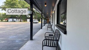 Een overdekt buitenterrein met een 'Cottage' bord, bankjes en uitzicht op de straat.