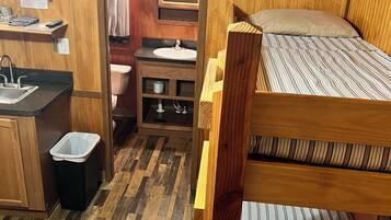 A compact, wooden-furnished room with bunk beds, a small kitchenette, a sink, and a mirror.