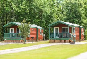 Two red cabins with green railings and porches, surrounded by trees.