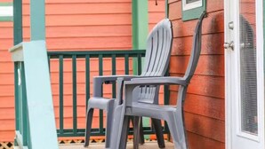 Un porche avec deux chaises et une petite table, une porte avec une fenêtre et une rambarde verte.
