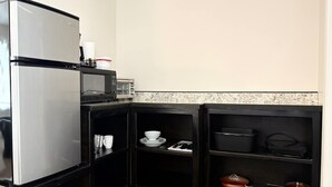 A compact kitchen with a stainless steel refrigerator, a microwave, and a toaster oven. There are shelves with dishes and cookware. - Room 8 at Inland Lakes Motel, Indian River, MI (Indian River)