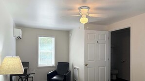 A bedroom with a bed, a chair, a desk, a ceiling fan, a window with blinds, and a door leading to a bathroom. - Room 8 at Inland Lakes Motel, Indian River, MI (Indian River)