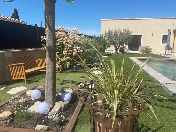 Un jardin aménagé avec une piscine, un banc en bois et un bac à fleurs en métal.
