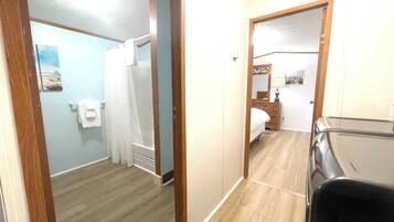 Een hotelkamer met een houten vloer, een bed, een dressoir, een spiegel en een douche.