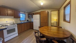 A compact kitchen with wooden cabinets, a white stove, and a dining table with chairs. - Star Gate Mobile Home 16 Indian River, MI (Indian River)
