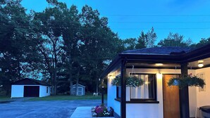 A small, single-story building with a covered porch, a garage, and a number '12' on the door. - Star Gate Mobile Home 16 Indian River, MI (Indian River)