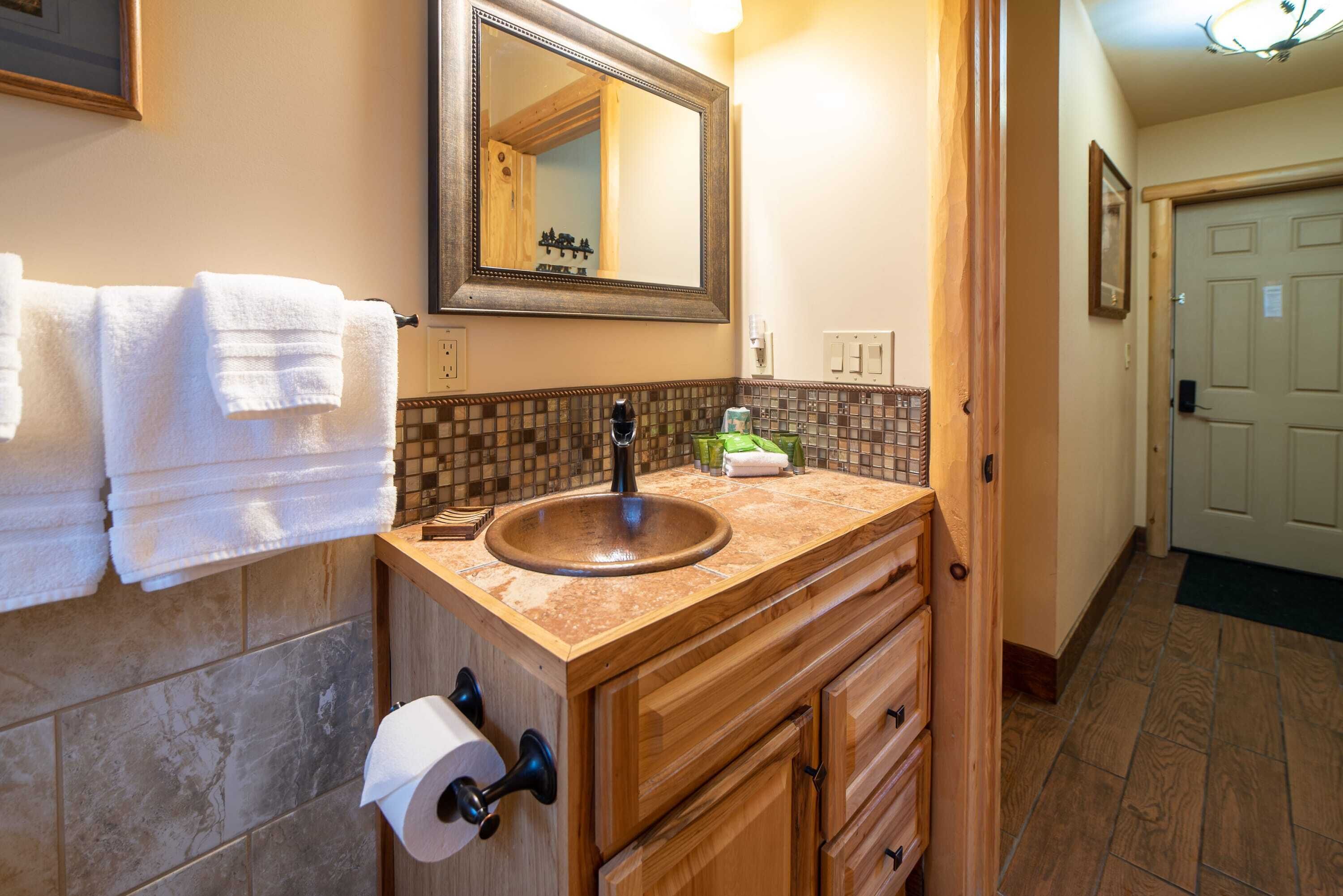 A bathroom with a wooden vanity, a sink, a mirror, and a towel rack.